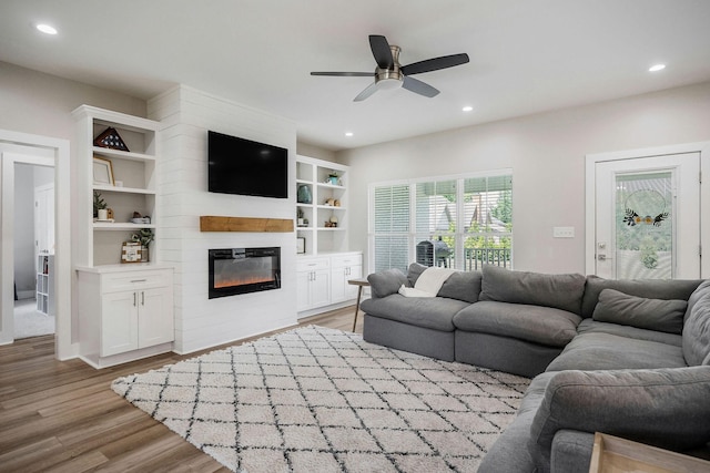 living room featuring a fireplace, built in shelves, ceiling fan, and light wood-type flooring