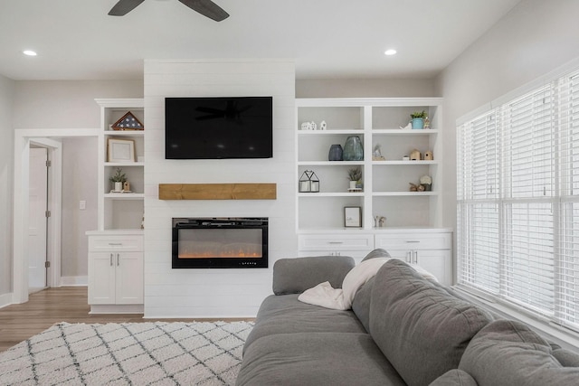 living room featuring light wood-type flooring, ceiling fan, and a fireplace