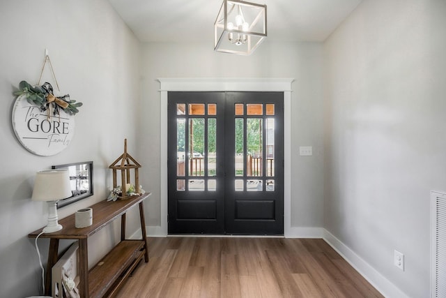 foyer entrance with wood-type flooring, french doors, and an inviting chandelier