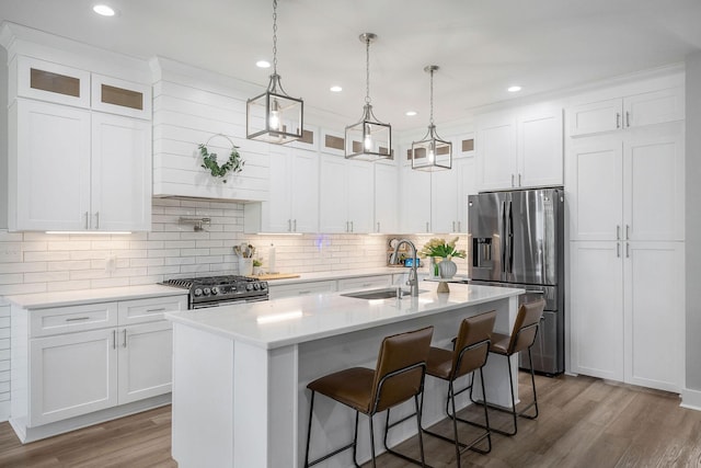 kitchen with appliances with stainless steel finishes, white cabinetry, sink, hanging light fixtures, and a kitchen island with sink