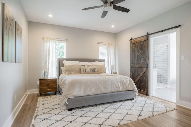 bedroom with light wood-type flooring, ceiling fan, a barn door, and ensuite bath