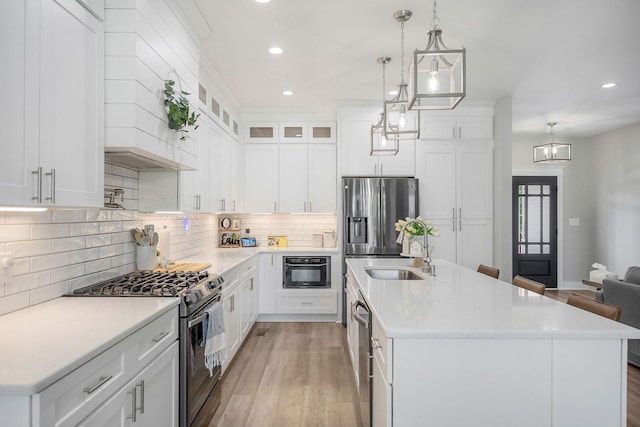 kitchen with decorative light fixtures, white cabinetry, a center island with sink, and appliances with stainless steel finishes