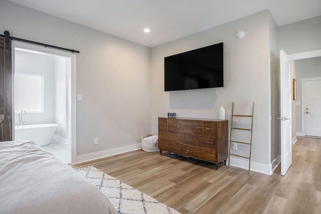 bedroom with a barn door, connected bathroom, and light hardwood / wood-style floors