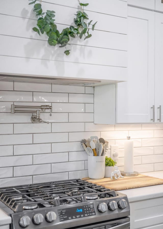 interior details with backsplash, white cabinets, and gas stove