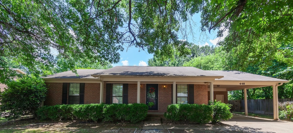 single story home featuring brick siding, concrete driveway, covered porch, fence, and an attached carport