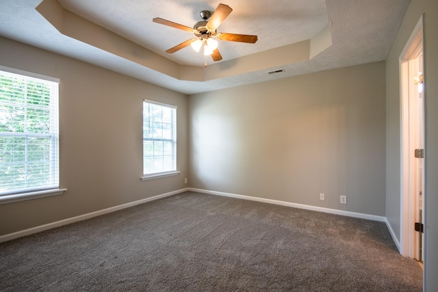 unfurnished room featuring ceiling fan, a raised ceiling, a textured ceiling, and dark carpet