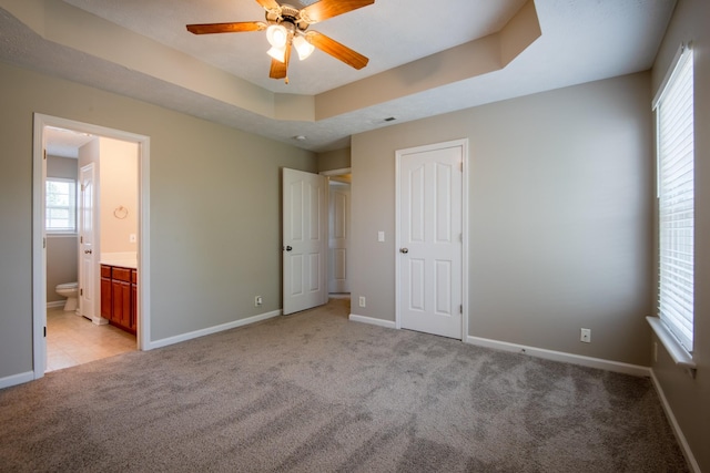 unfurnished bedroom featuring a raised ceiling, connected bathroom, ceiling fan, and light colored carpet