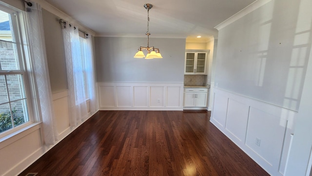 unfurnished dining area featuring a healthy amount of sunlight, crown molding, dark hardwood / wood-style flooring, and a chandelier