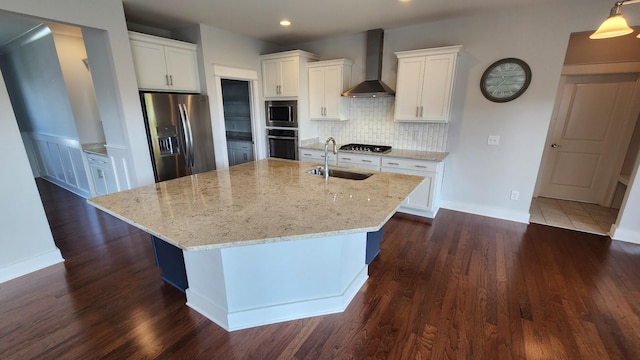 kitchen featuring a kitchen island with sink, white cabinets, wall chimney range hood, and appliances with stainless steel finishes