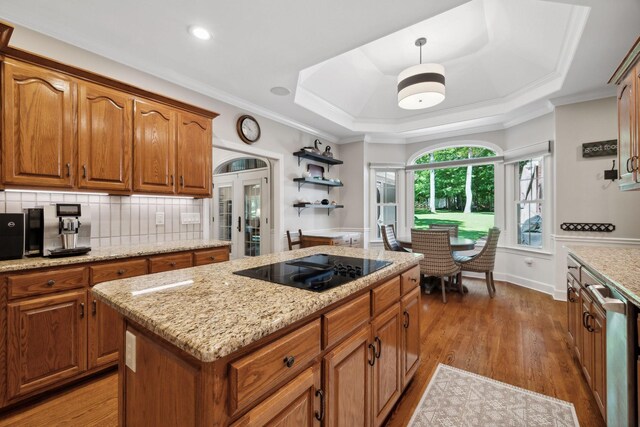 kitchen featuring a tray ceiling, light stone counters, black electric cooktop, hardwood / wood-style floors, and tasteful backsplash