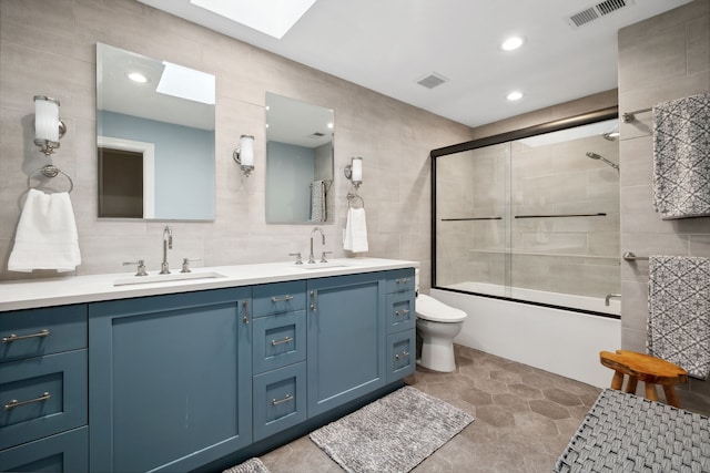 full bathroom with double vanity, shower / bath combination with glass door, tile floors, tile walls, and toilet