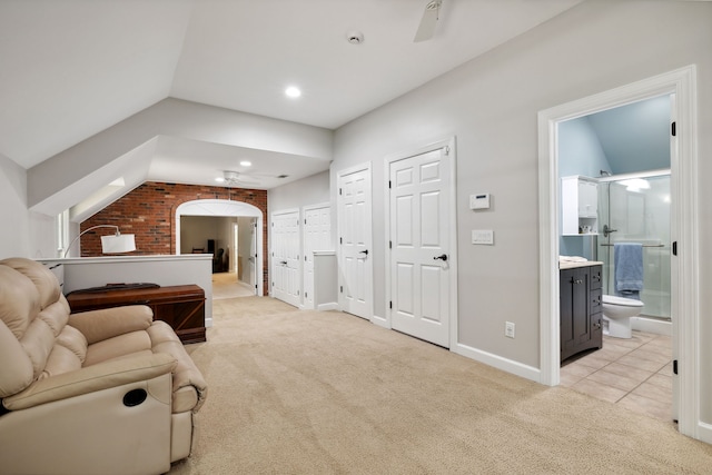 tiled bedroom featuring brick wall, lofted ceiling, two closets, and connected bathroom