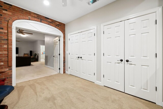 hallway featuring light colored carpet and brick wall