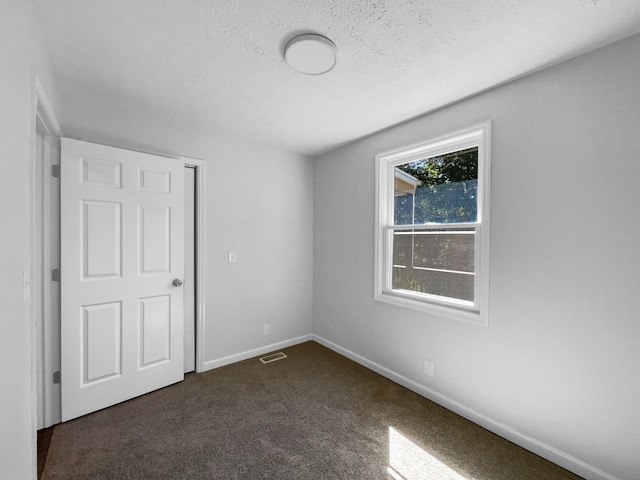 unfurnished bedroom featuring a textured ceiling and dark colored carpet