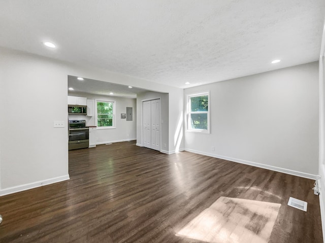 unfurnished living room with plenty of natural light, dark hardwood / wood-style floors, a textured ceiling, and electric panel