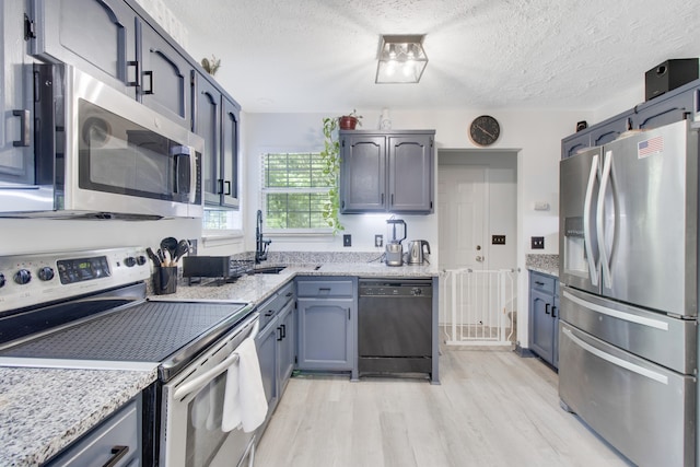 kitchen with stainless steel appliances, light hardwood / wood-style floors, sink, light stone countertops, and a textured ceiling