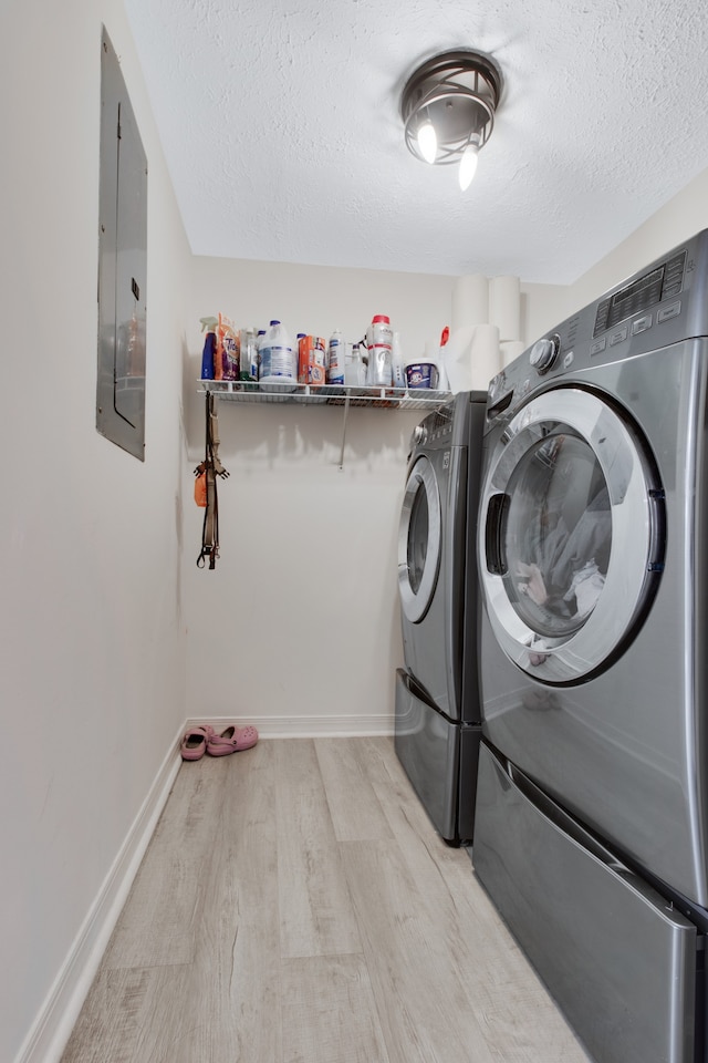 laundry room featuring light wood-type flooring, a textured ceiling, separate washer and dryer, and electric panel