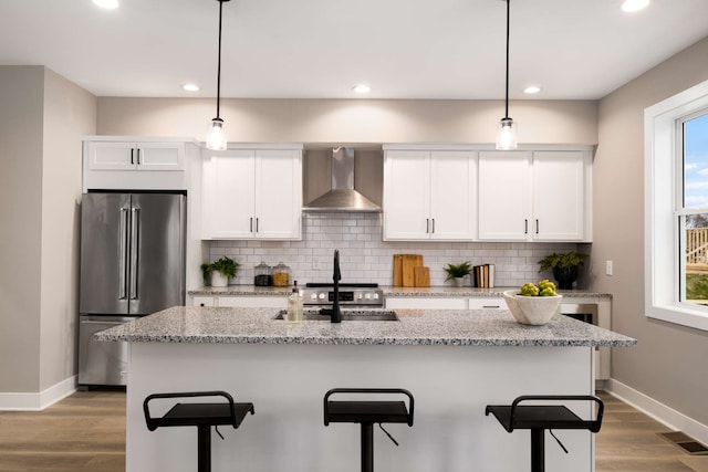 kitchen with wall chimney range hood, hardwood / wood-style flooring, a healthy amount of sunlight, and stainless steel appliances