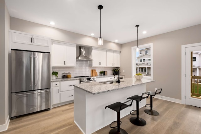 kitchen featuring light wood-type flooring, wall chimney exhaust hood, white cabinets, sink, and appliances with stainless steel finishes