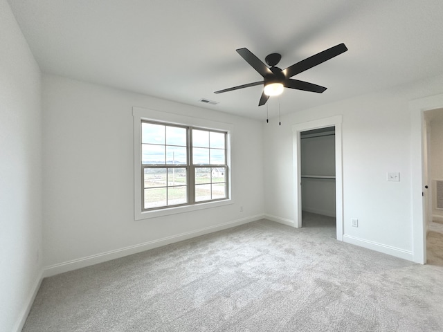 unfurnished bedroom featuring ceiling fan, light colored carpet, a walk in closet, and a closet