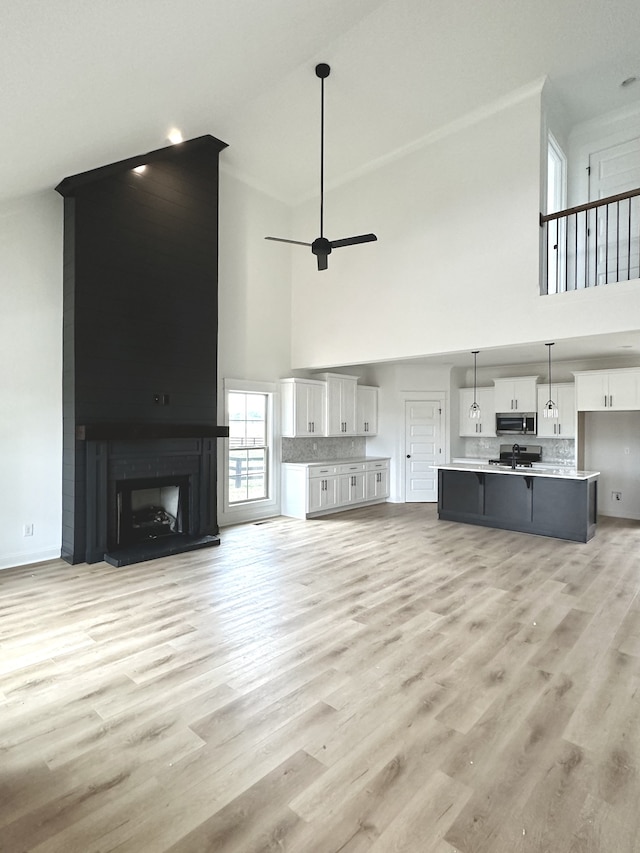 unfurnished living room featuring a fireplace, light wood-type flooring, a towering ceiling, and ceiling fan