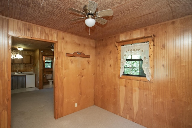 carpeted spare room featuring a notable chandelier, wood walls, wood ceiling, and sink