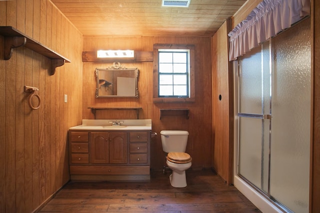 bathroom featuring vanity, wooden walls, hardwood / wood-style flooring, toilet, and walk in shower