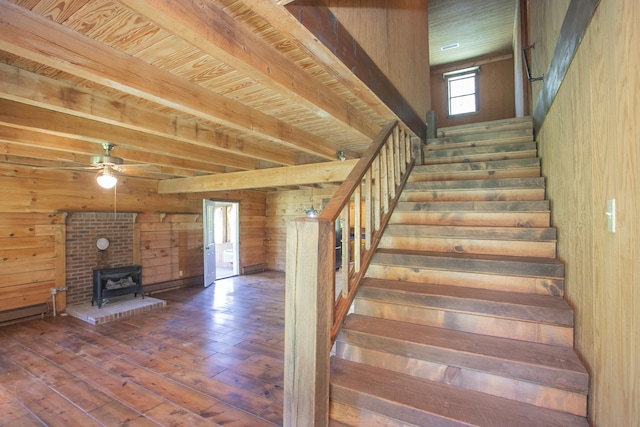 stairs with ceiling fan, hardwood / wood-style flooring, wooden ceiling, a wood stove, and wood walls