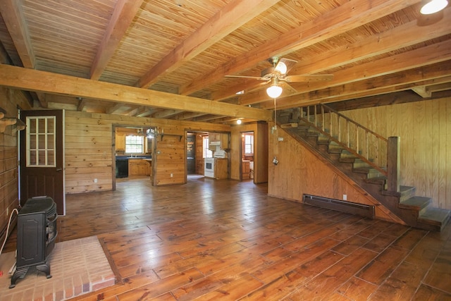 unfurnished living room with ceiling fan, a baseboard heating unit, wooden walls, beamed ceiling, and a wood stove