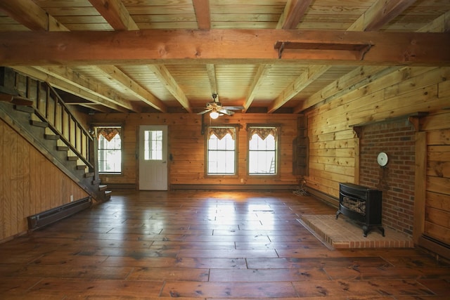 unfurnished living room with beam ceiling, a wood stove, ceiling fan, a baseboard radiator, and wooden walls