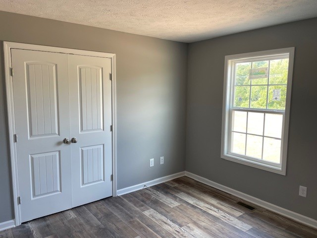 unfurnished bedroom featuring a textured ceiling, dark hardwood / wood-style flooring, and a closet