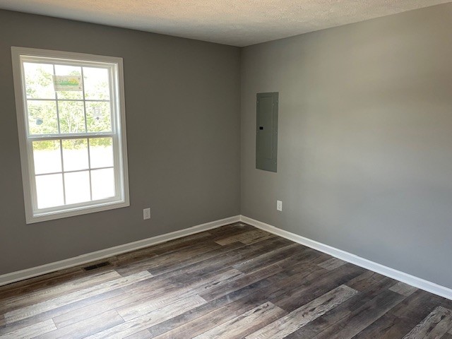 empty room featuring hardwood / wood-style flooring, electric panel, and a textured ceiling