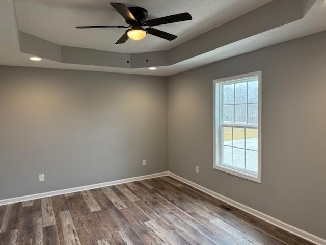 empty room with ceiling fan, a tray ceiling, and hardwood / wood-style floors