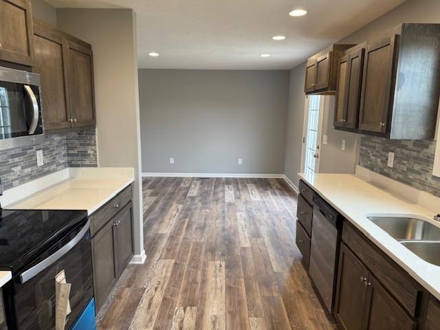 kitchen featuring sink, dark wood-type flooring, backsplash, dark brown cabinets, and stainless steel appliances