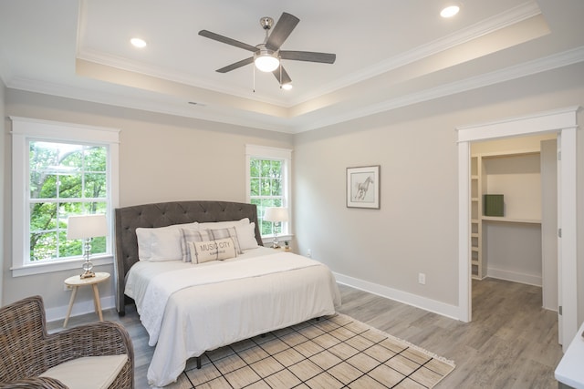 bedroom featuring a raised ceiling, multiple windows, crown molding, and light hardwood / wood-style flooring