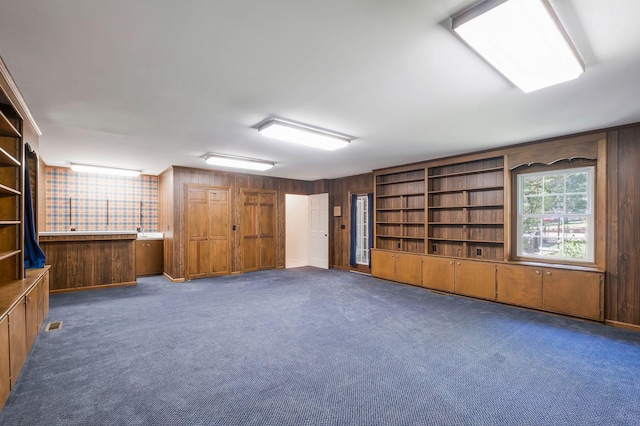 interior space with built in shelves, wood walls, and dark carpet