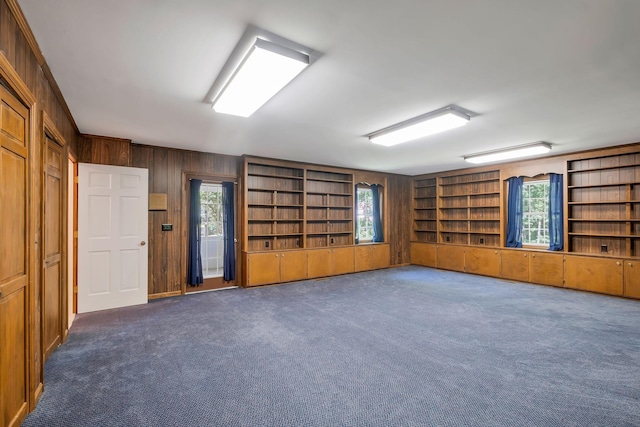 interior space featuring built in shelves, wood walls, and dark carpet