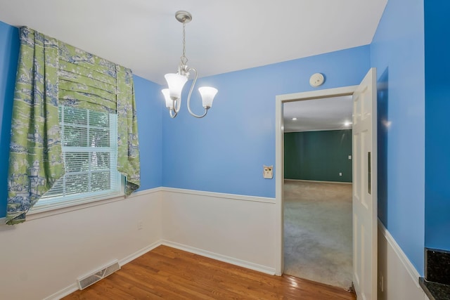 empty room with wood-type flooring and a notable chandelier