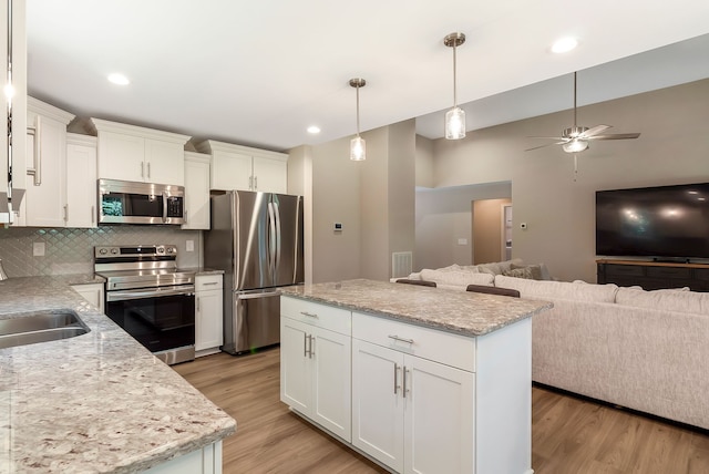 kitchen with ceiling fan, light hardwood / wood-style flooring, stainless steel appliances, backsplash, and a center island