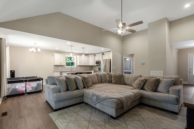 living room featuring sink, a high ceiling, light hardwood / wood-style floors, and ceiling fan with notable chandelier