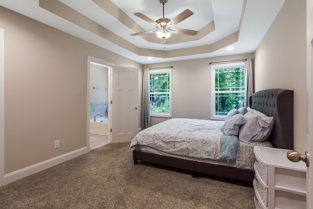 bedroom with dark carpet, ceiling fan, ensuite bath, and a tray ceiling