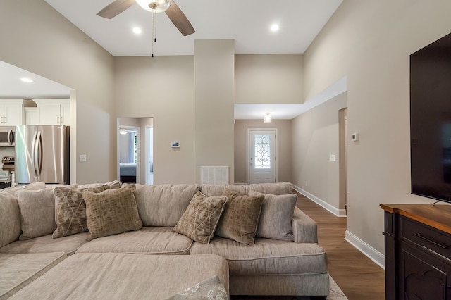 living room featuring wood-type flooring, a towering ceiling, and ceiling fan