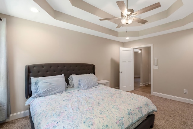 carpeted bedroom with ceiling fan and a raised ceiling