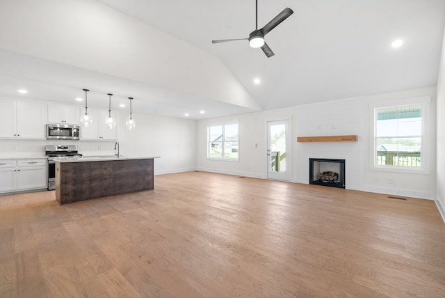 living room with ceiling fan, high vaulted ceiling, a fireplace, and light hardwood / wood-style floors