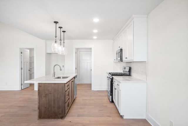 kitchen with sink, appliances with stainless steel finishes, white cabinetry, an island with sink, and decorative light fixtures