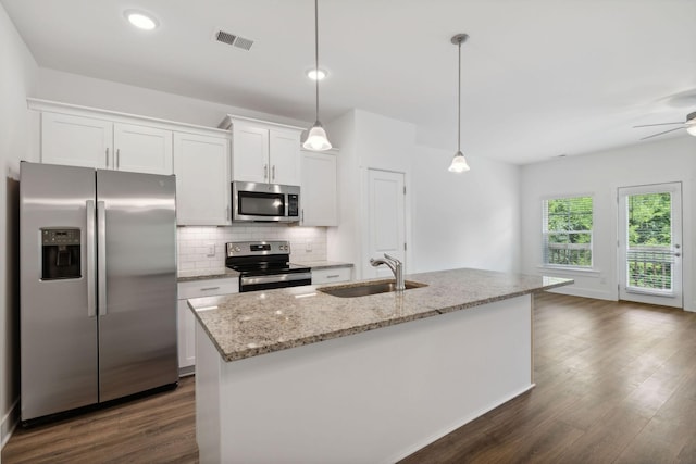 kitchen with appliances with stainless steel finishes, pendant lighting, sink, white cabinetry, and a kitchen island with sink