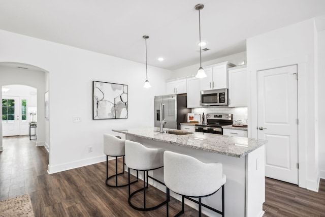 kitchen with backsplash, dark wood-type flooring, white cabinetry, appliances with stainless steel finishes, and a center island with sink