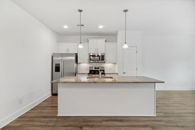 kitchen featuring hardwood / wood-style floors, decorative backsplash, light stone countertops, a kitchen island with sink, and stainless steel appliances