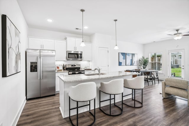 kitchen with sink, light stone counters, white cabinetry, stainless steel appliances, and a kitchen island with sink