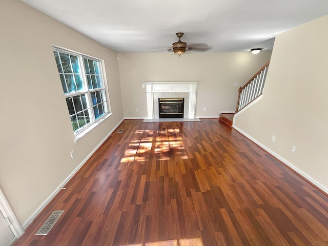 unfurnished living room featuring ceiling fan, dark wood-type flooring, and a tiled fireplace